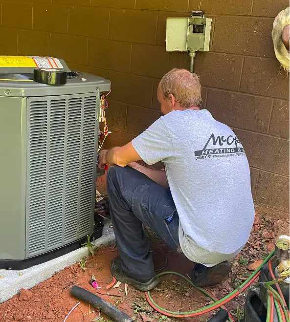 A friendly McGee Heating & Air technician, wearing a branded gray t-shirt, provides professional maintenance on an outdoor air conditioning unit.