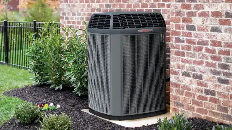 A professional installation of a Trane air conditioning unit on a concrete pad by the McGee team, located next to a brick wall.